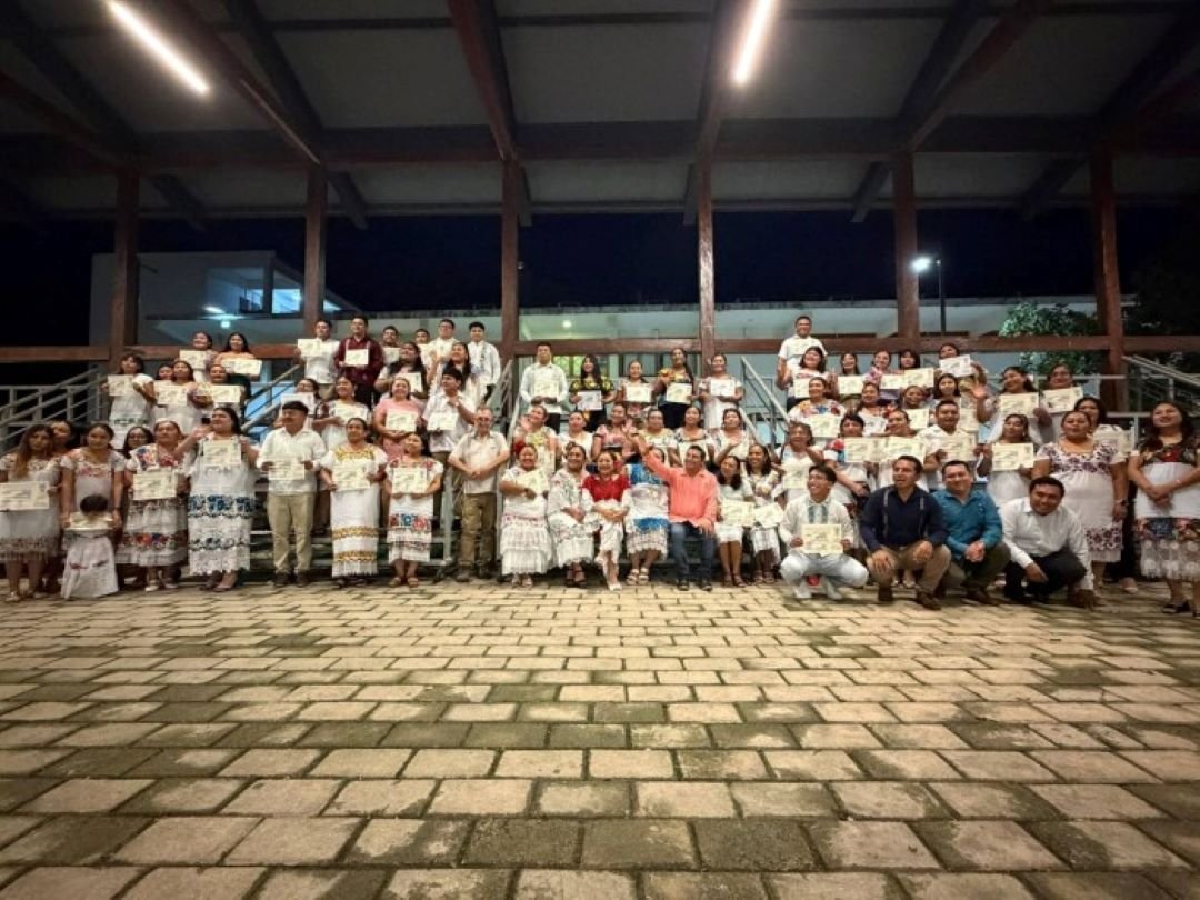 People gathered at a radio station event with banners celebrating 27 years of broadcasting in Maya language