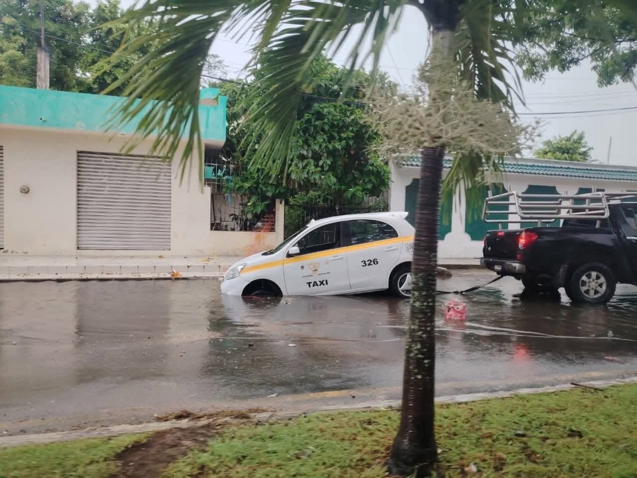 A taxi with its front end submerged in a water-filled excavation on a flooded street in Chetumal