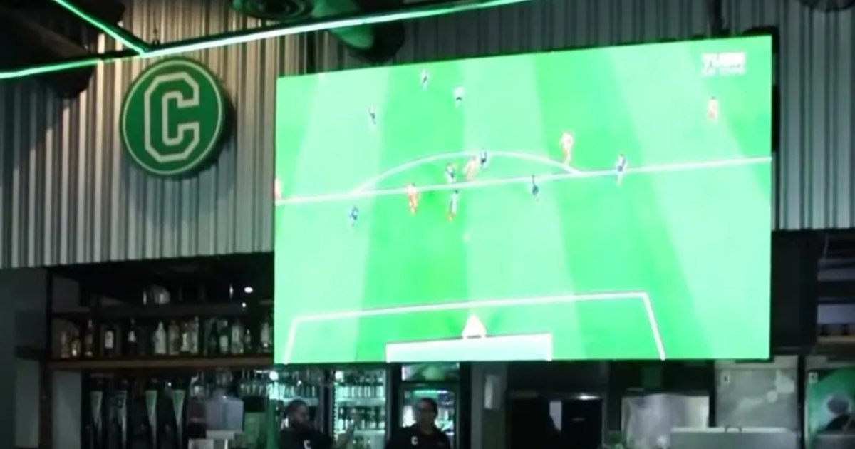 A bar or restaurant showing a soccer match on a large screen, with customers watching.
