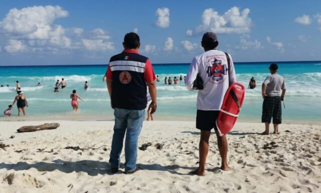 Cancún beach at dusk with people swimming despite warning signs