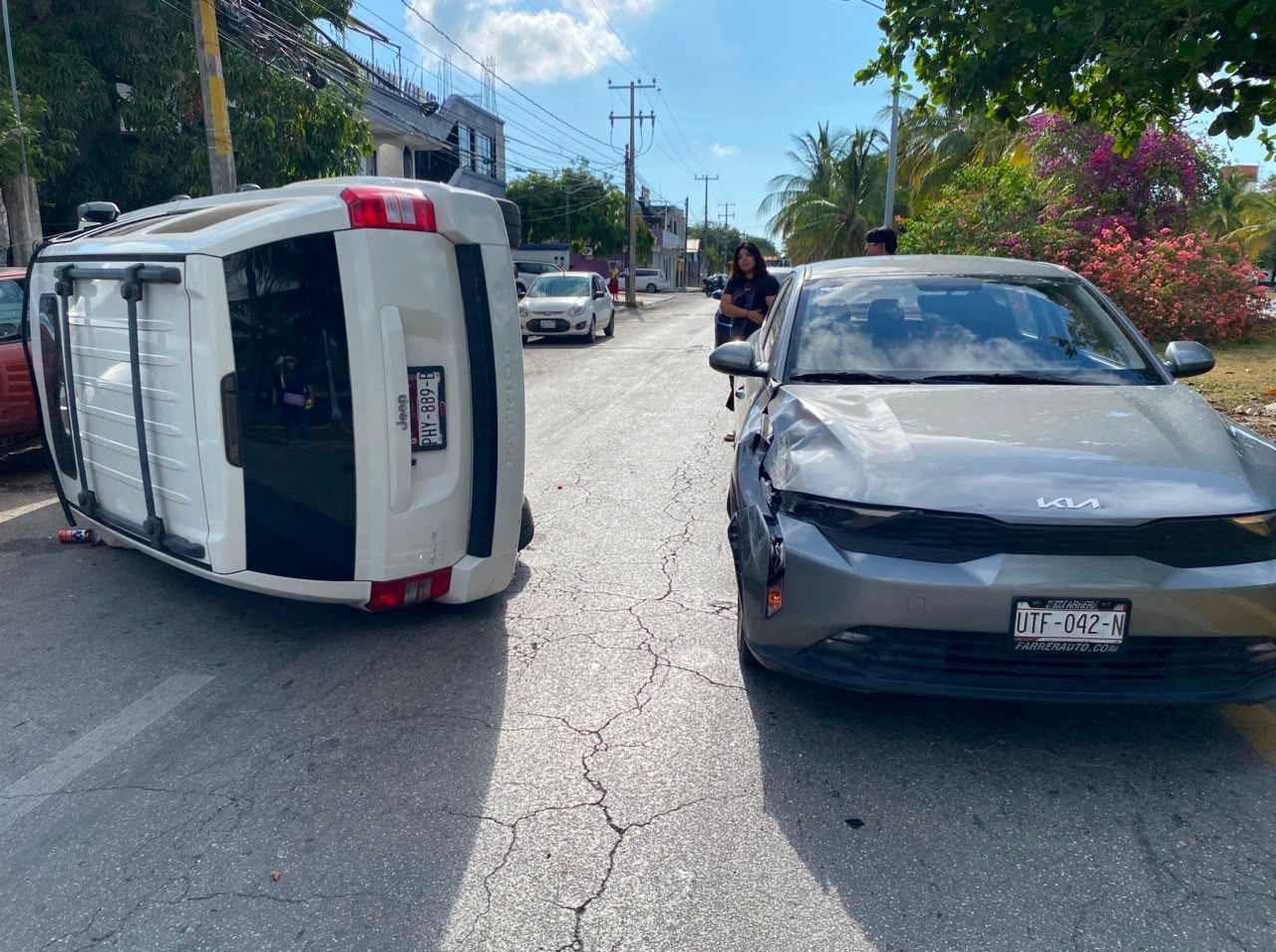 A silver Jeep overturned on a Cancun street after crashing into multiple parked cars, with debris scattered on the road.
