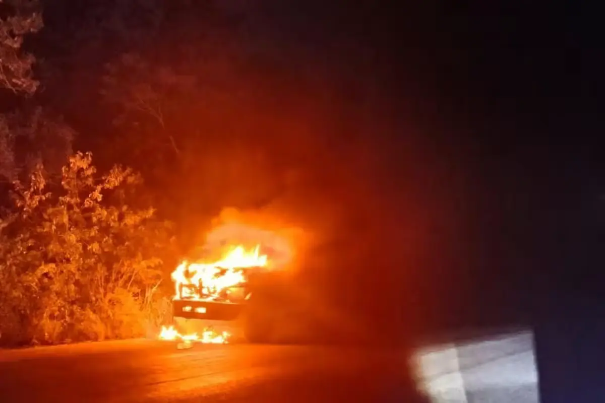 A dump truck fully engulfed in flames on the side of the Tulum-Cobá highway at night