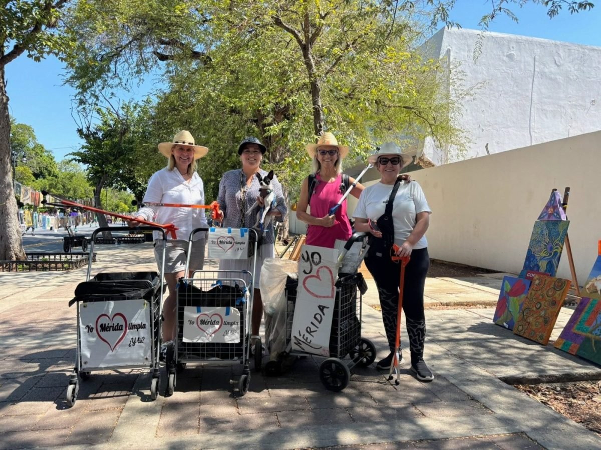 A foreign woman pushing a cart labeled 'Yo amo Mérida limpia' while picking up trash on a street in Merida's historic center.