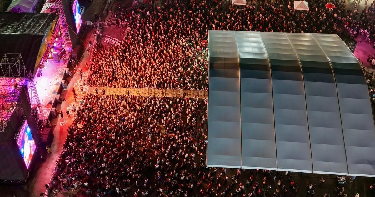Large crowd of people at a nighttime concert with stage lights and Grupo Mojado performing