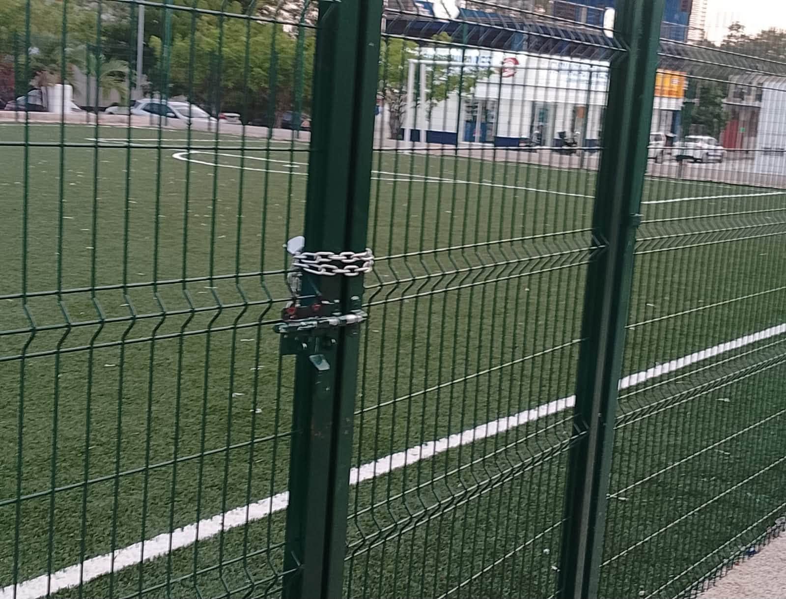 A locked gate at a sports field in Chetumal, Quintana Roo, with a padlock and chain preventing entry.