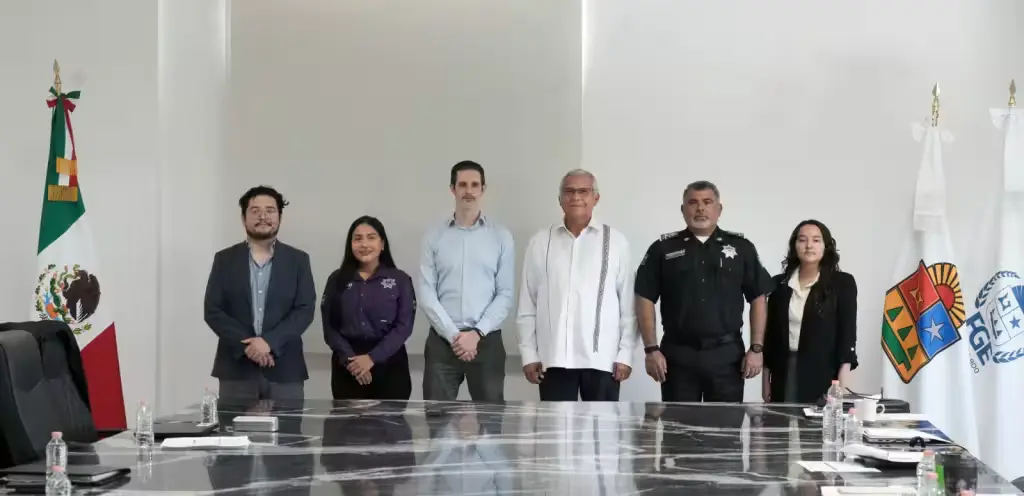 A group photo of local authorities and officials standing together in a conference room with flags and a large table.$# CAPTION