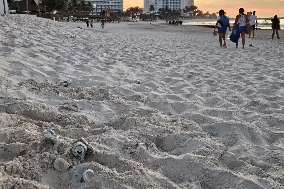 Beer cans and snack wrappers scattered on the sand at Playa Gaviotas beach in Cancun early in the morning