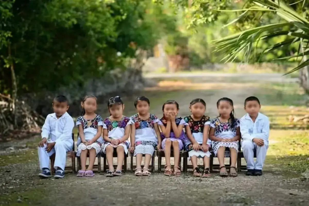 Children in traditional Maya clothing, including huipil dresses for girls and manta shirts for boys, in a classroom setting.