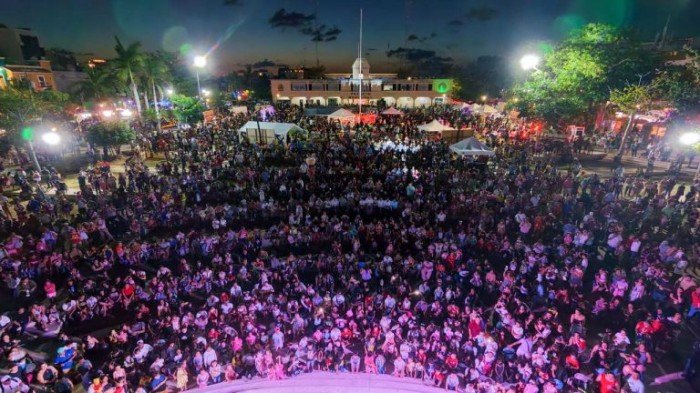 A large crowd gathered in a plaza watching a football match on a giant screen