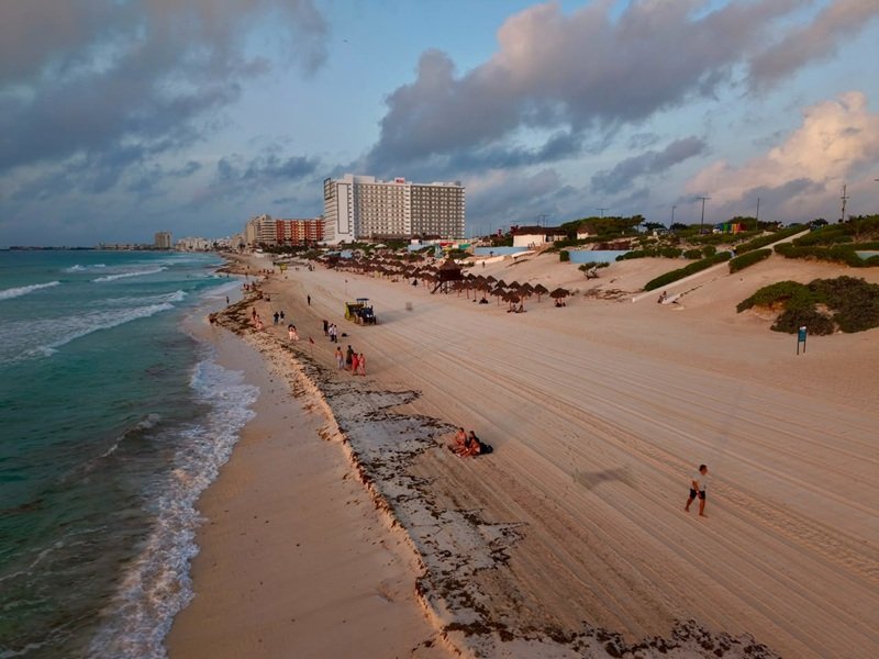 Tourists on a beach in the Mexican Caribbean with sargassum washed ashore, amid concerns about reduced flights for the summer season.