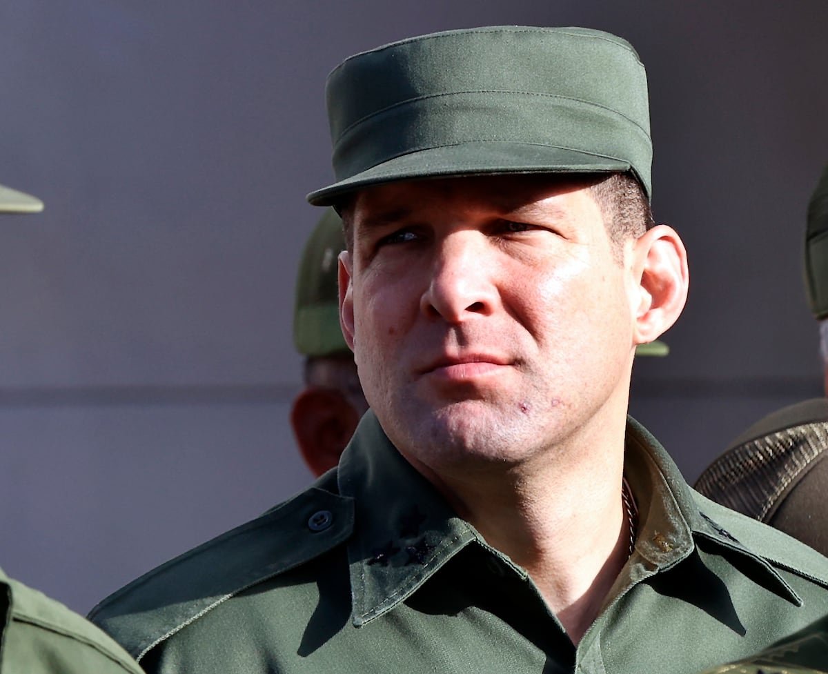 A military officer wearing a green uniform and cap, with a serious expression on his face.$# CAPTION