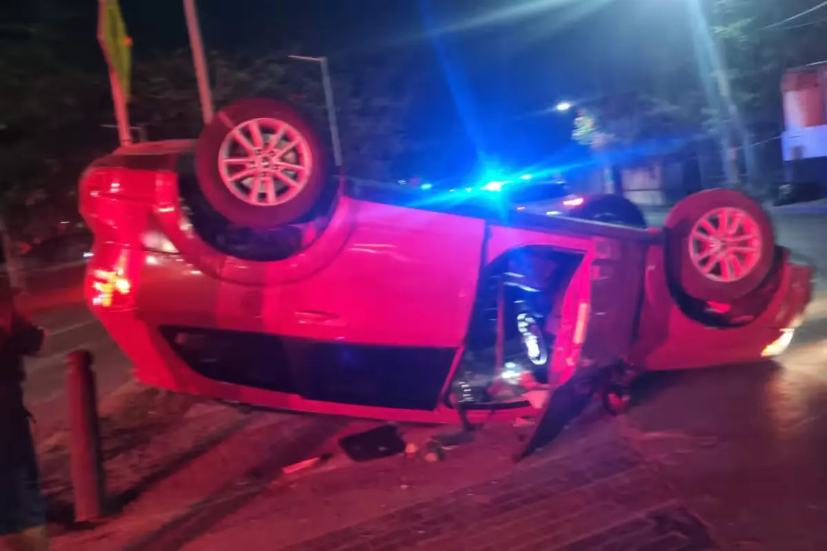 National Guard officers and Red Cross paramedics stand near an overturned red Dodge Journey at a Cancún intersection after a crash that injured three people.