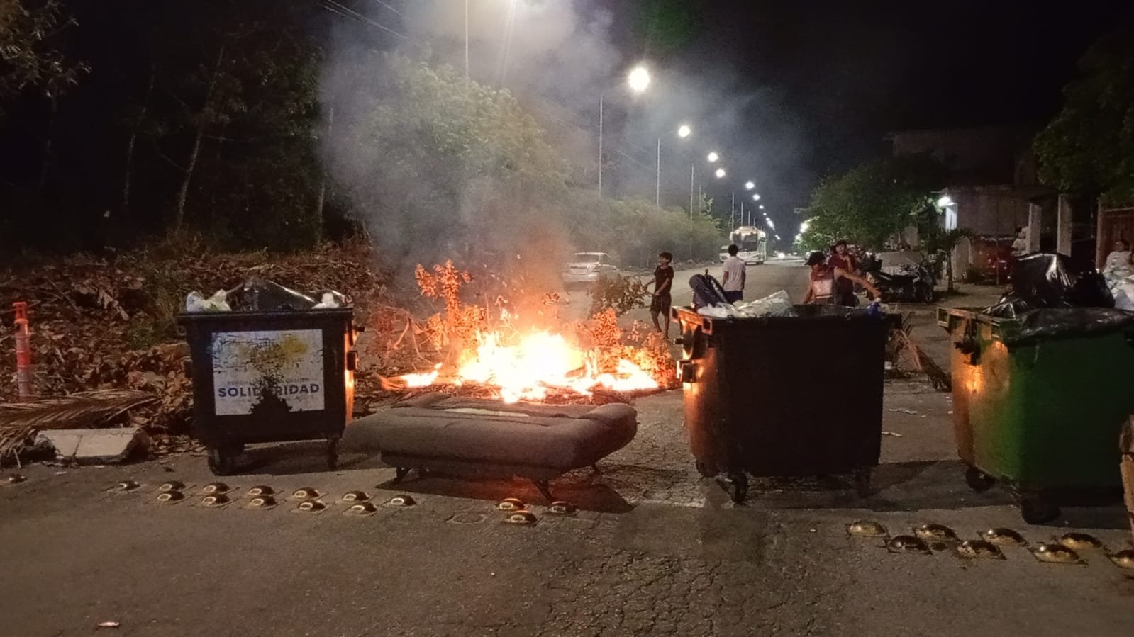 Residents block Avenida Loros in Villas del Sol with burning branches and tires during a protest over a three-day power outage.