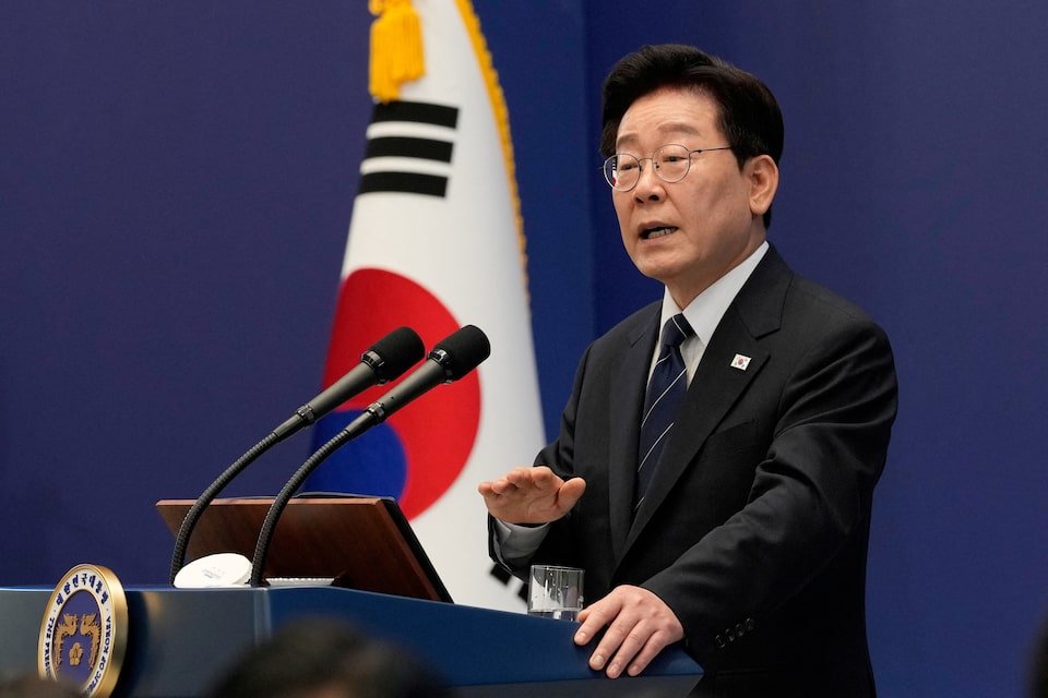 A man wearing glasses and a dark suit speaks at a podium, with a South Korean flag in the background. He gestures as he delivers a speech.$# CAPTION