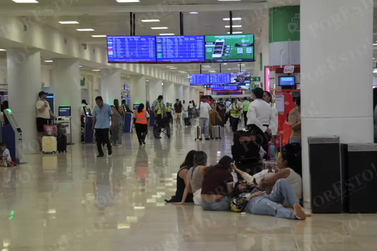 Travelers with luggage waiting in a crowded terminal at Cancún International Airport