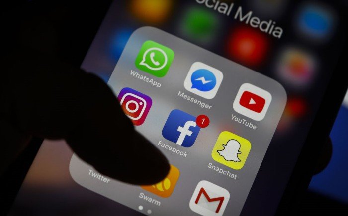 Children gathered around a smartphone with social media apps on screen