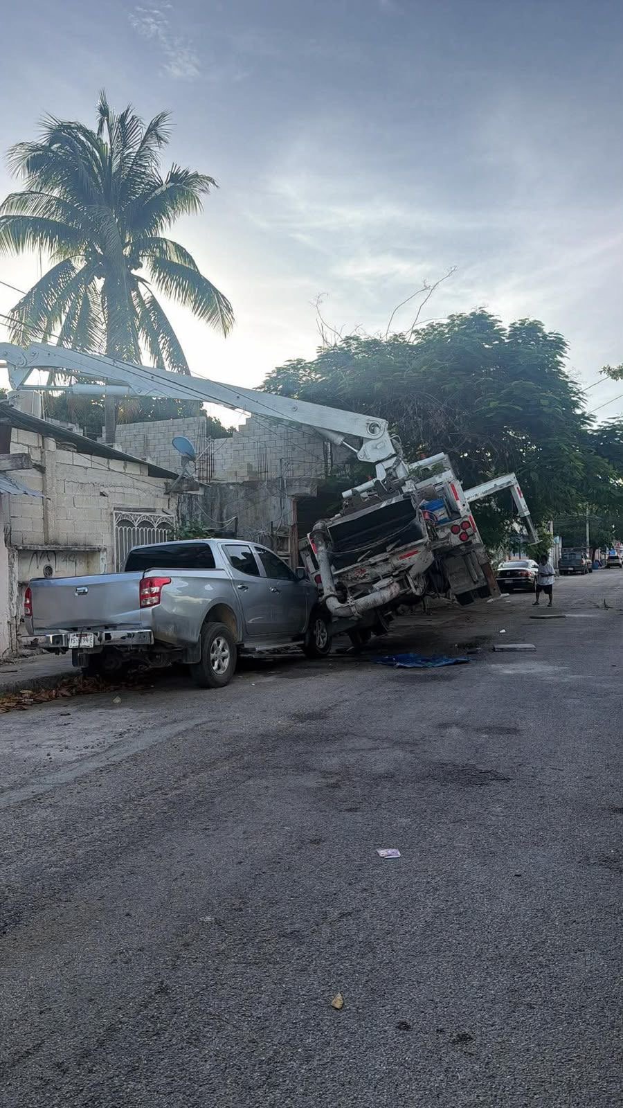 A concrete pump truck leans against a parked pickup truck after nearly tipping over in a Playa del Carmen neighborhood.