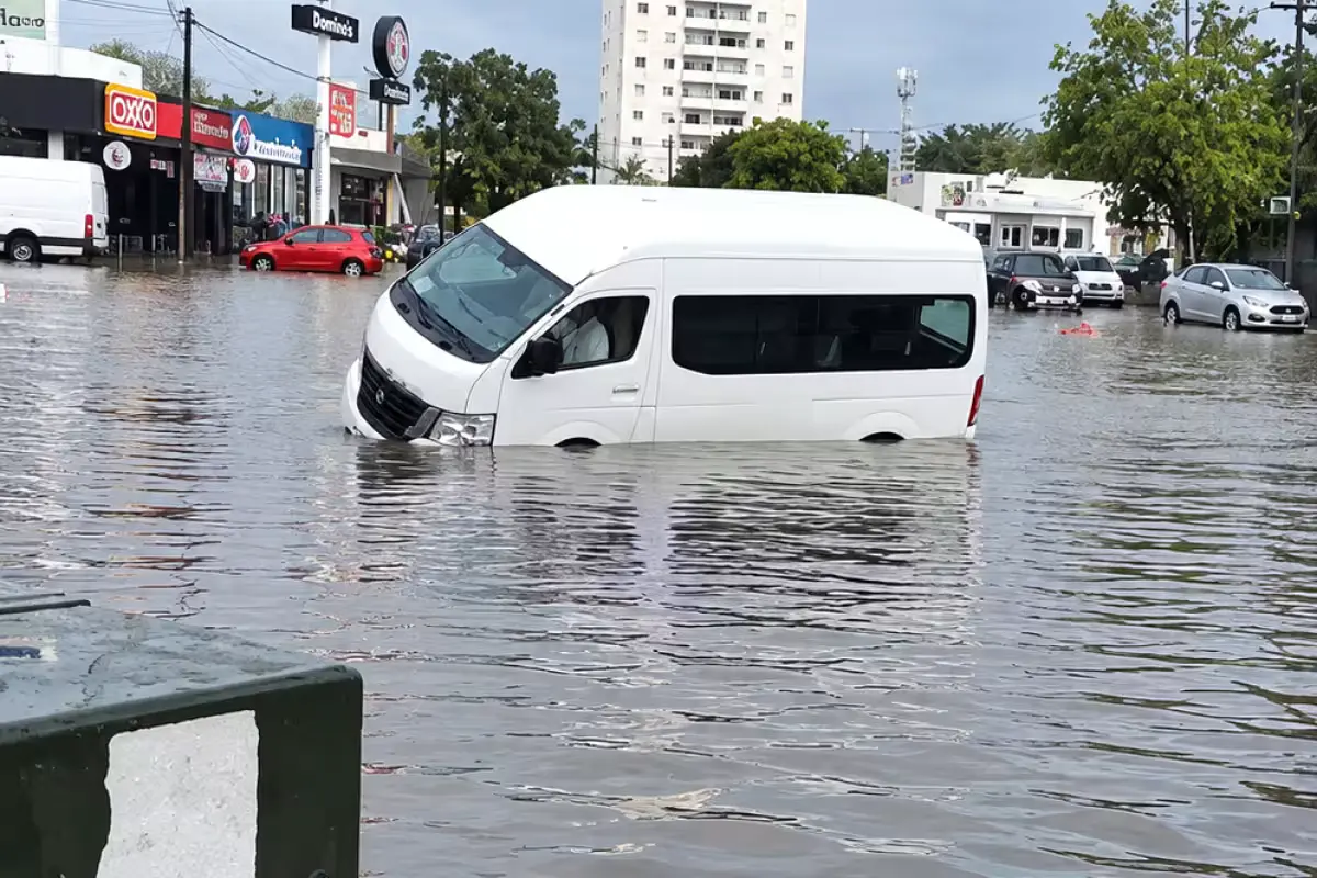 Downed Federal Electricity Commission pole lying across damaged parked vehicles on a flooded street in Cancún, Quintana Roo