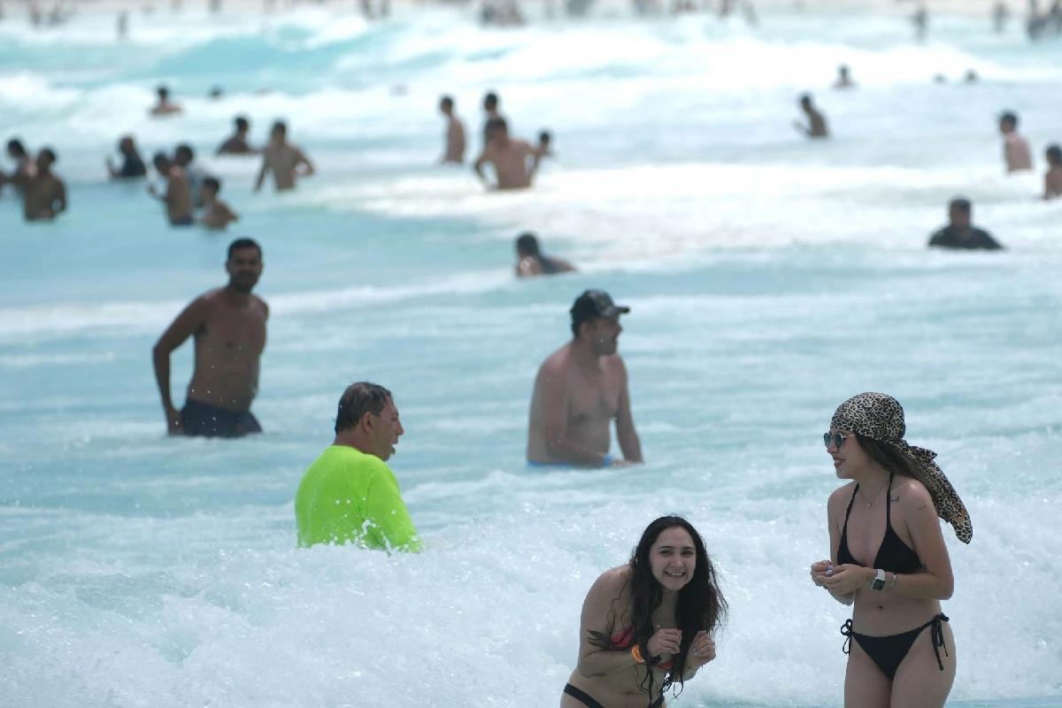 Tourists relaxing on a beach in Cancun, with hotels in the background
