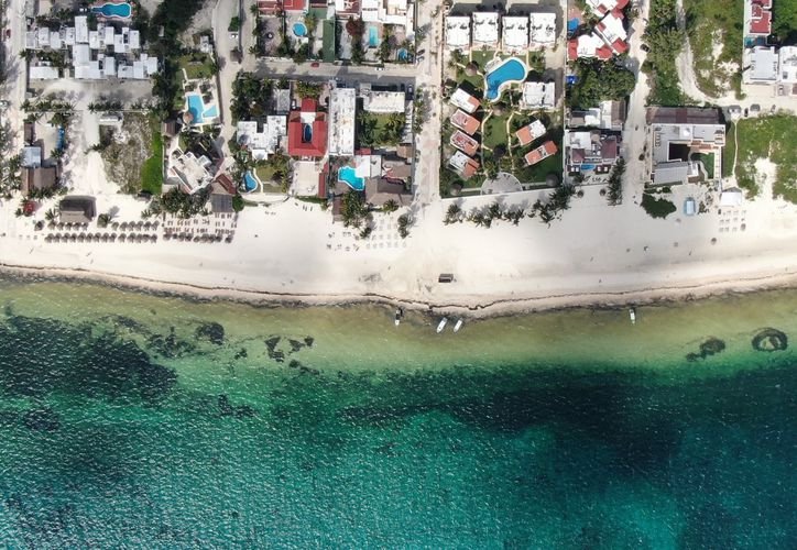 An aerial photograph shows white sand beach lined with resort buildings and swimming pools beside clear turquoise and dark blue water.