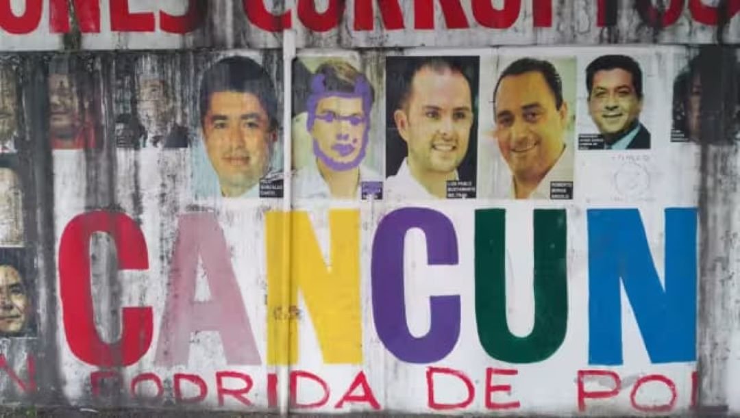 A weathered wall poster displays the word CANCUN in large multicolored letters below a row of six portraits of men, with one face scribbled over in purple.
