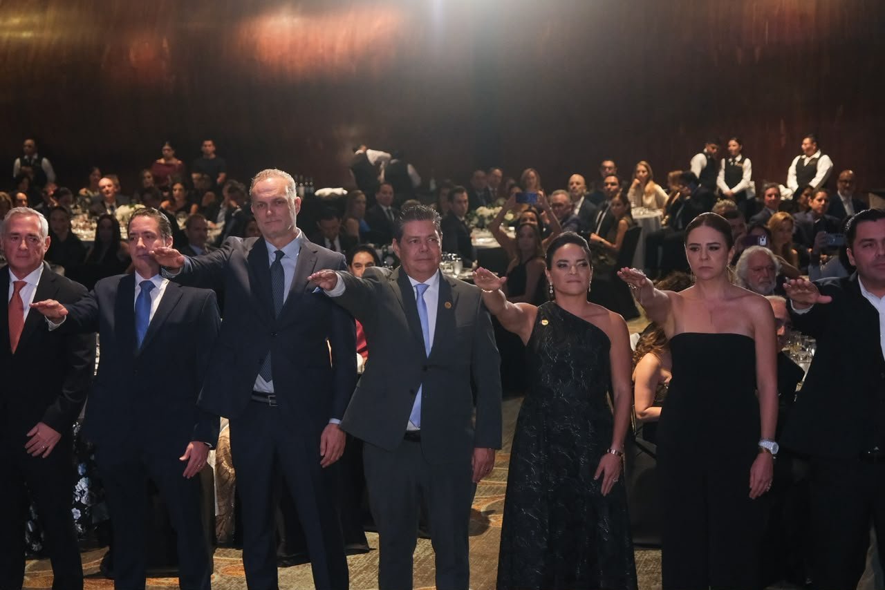 A group of individuals taking an oath during a formal ceremony, surrounded by an audience in an event setting.$# CAPTION