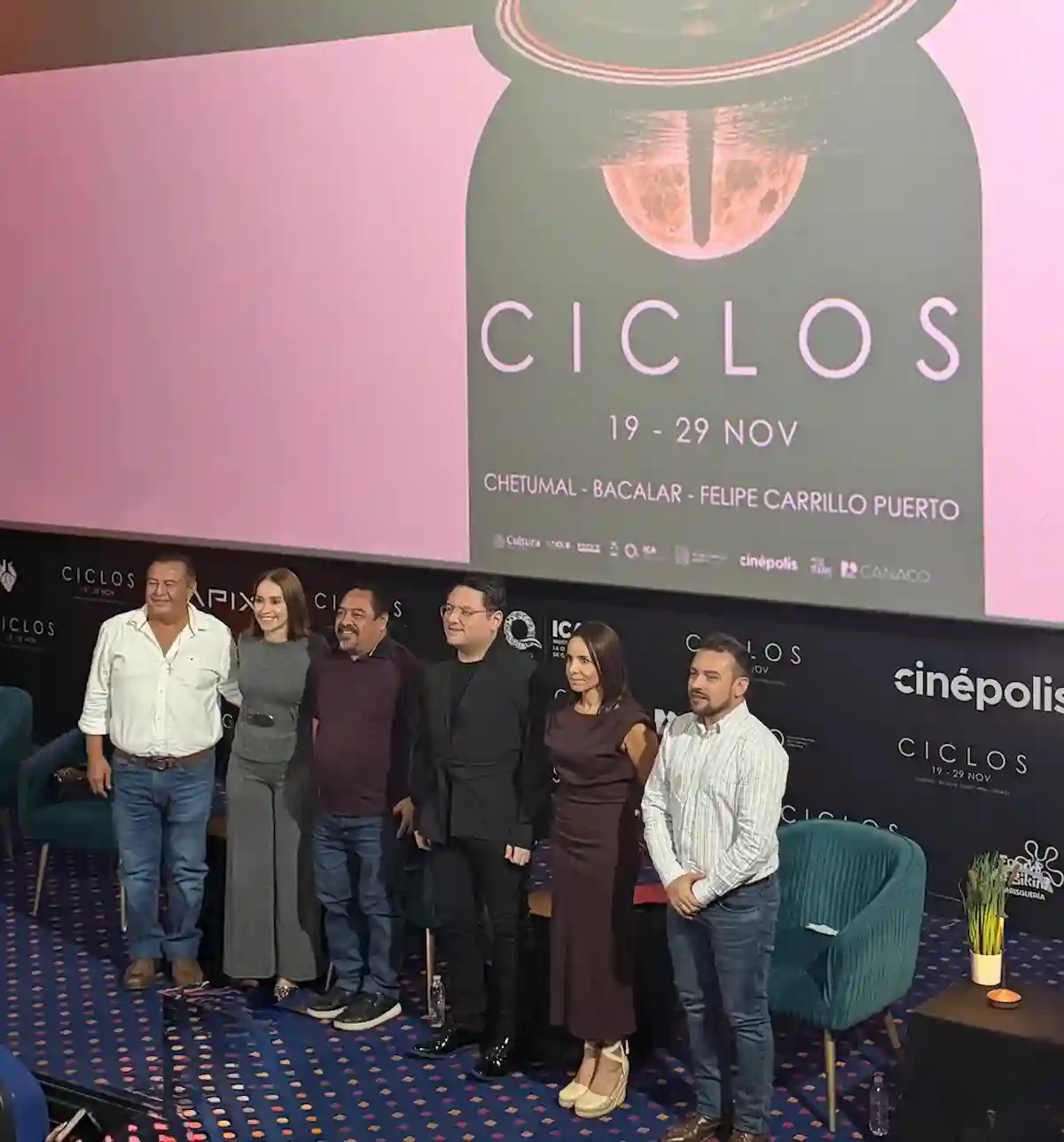 A group of six individuals standing in front of a large screen displaying the "CICLOS" film festival banner at a press conference. The individuals appear to be part of the festival team or guests.$# CAPTION
