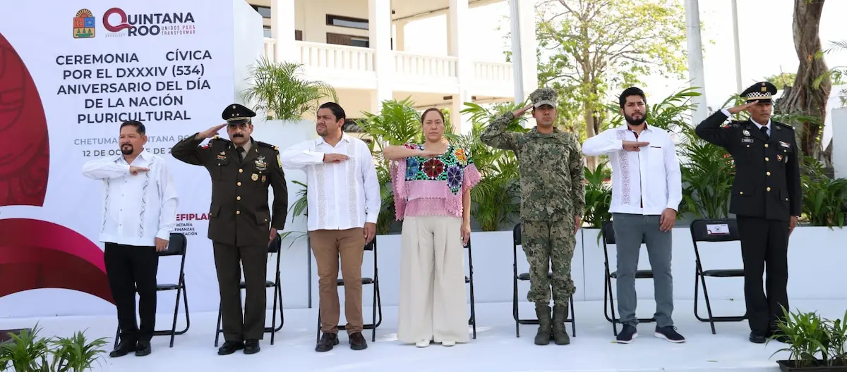 Officials participating in a civic ceremony, saluting while standing on stage in front of a banner in Quintana Roo, Mexico.$# CAPTION