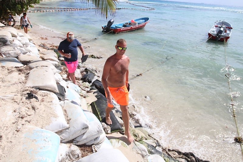 People working at the beach with sandbags and boats in the water
