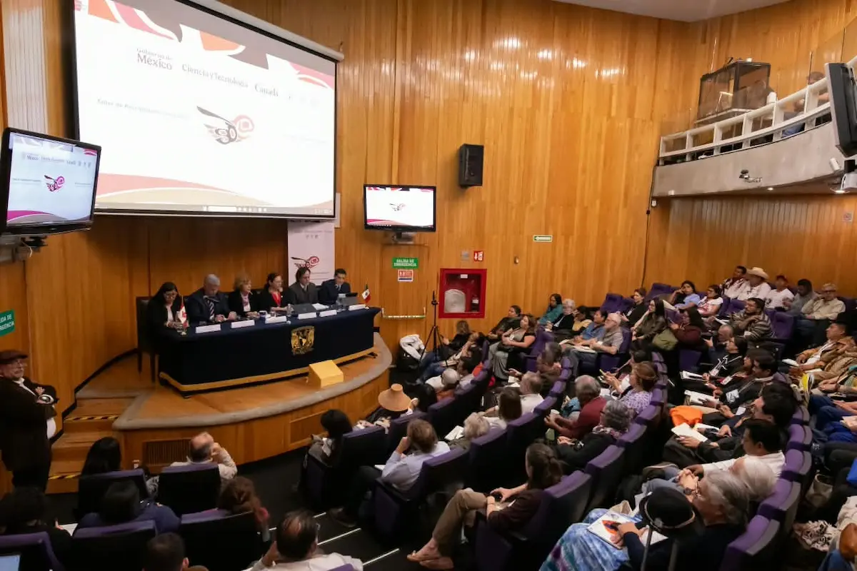 A conference session taking place in a lecture hall with a panel of speakers and an audience in attendance.$# CAPTION