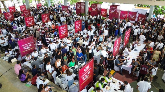 A large crowd of people gathers in an open covered area with many red banners and tables set up for what appears to be a registration or voting event.