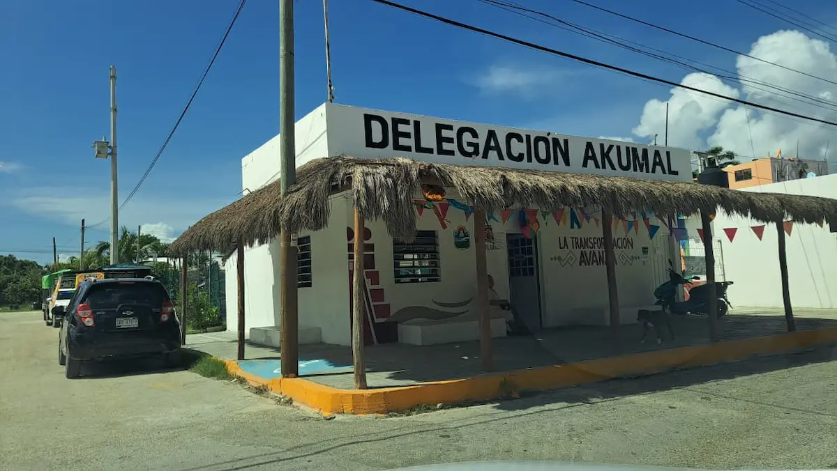 A view of a delegation building with a thatched roof and colorful bunting in Akumal, Mexico on a sunny day.$