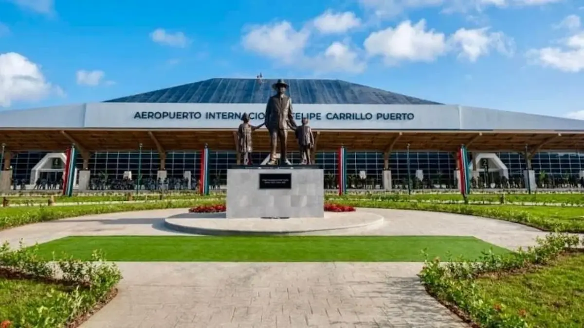 Front view of Felipe Carrillo Puerto International Airport with a statue in the foreground and cloudy blue sky above
