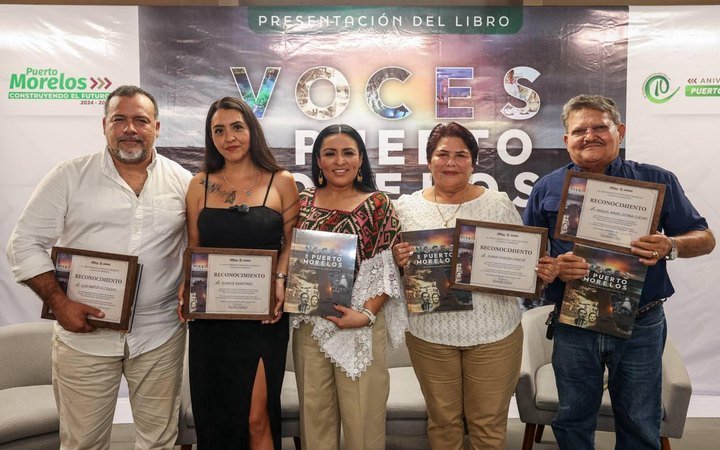 Five people stand side by side holding framed certificates and copies of a book in front of a banner reading Presentacion del Libro Voces de Puerto Morelos.