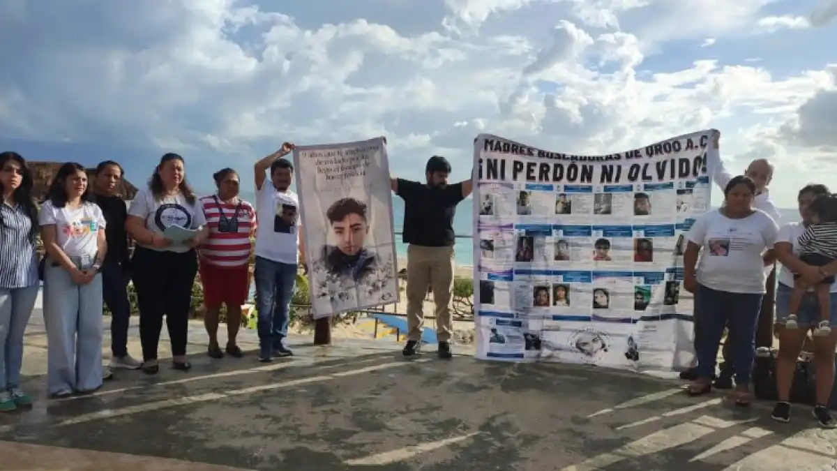 A group of people stands outdoors holding two large banners, one with a portrait and text and another covered with photographs and the words Ni Perdon Ni Olvido.