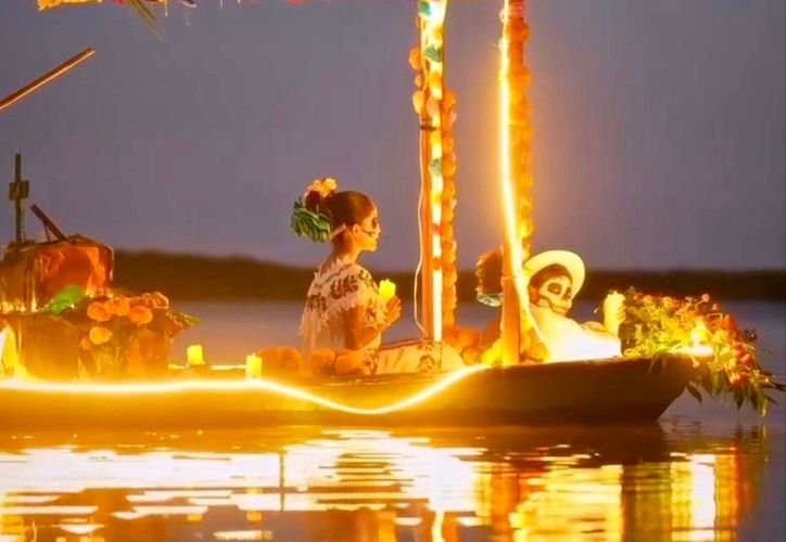 A small boat decorated with flowers and glowing lights carries two people, one wearing a flower in her hair and another with a skull-like face, across dark water at dusk.