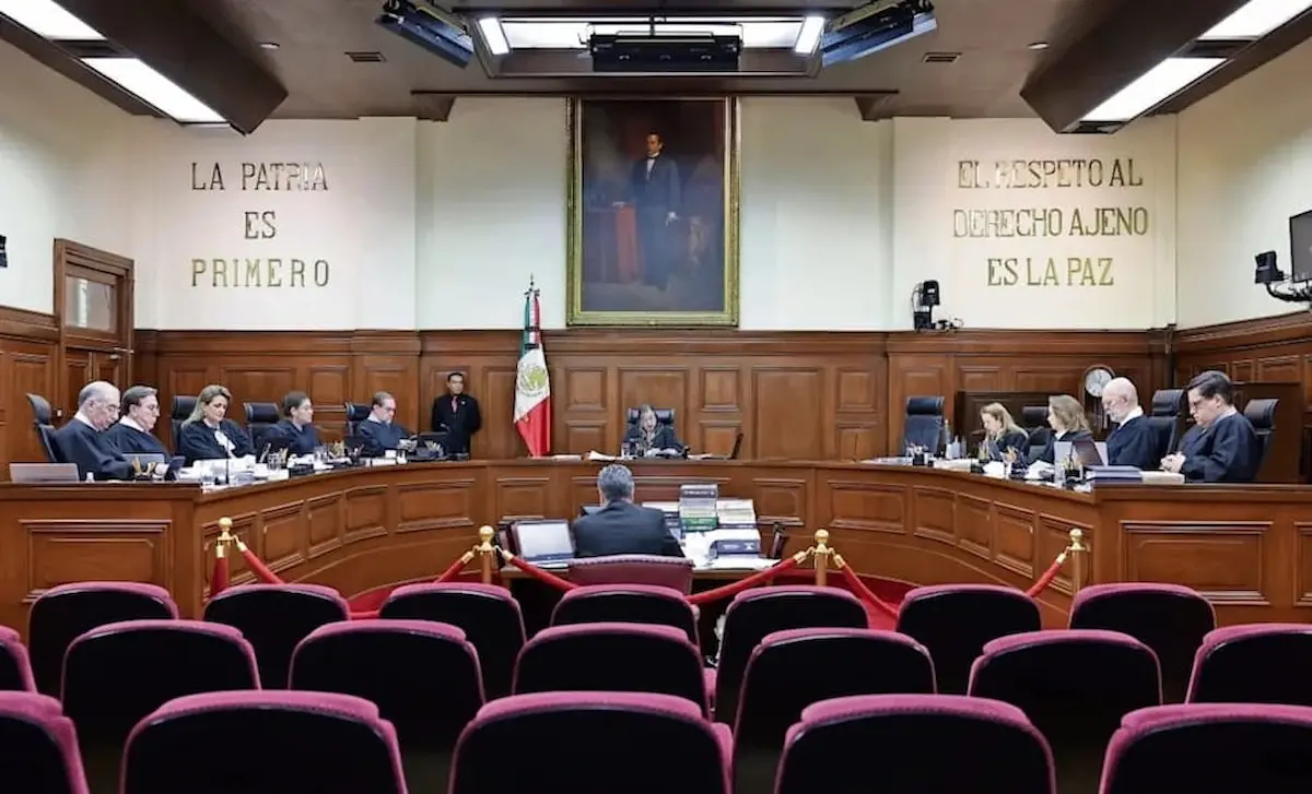 A view of the Mexican Supreme Court with judges in session, featuring a national flag and prominent paintings on the walls.$#$ CAPTION