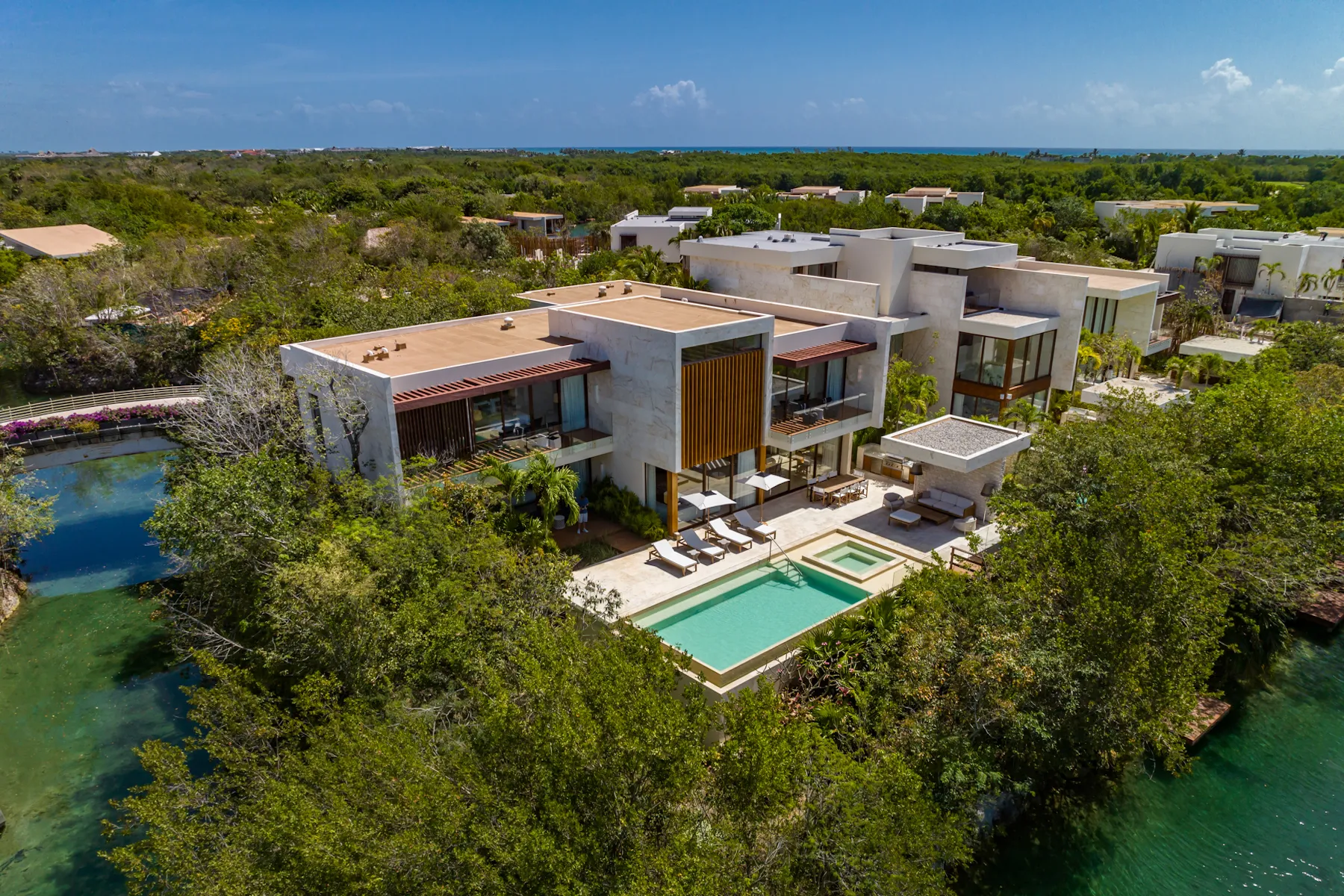 Aerial view of a modern villa with a pool, surrounded by lush greenery and waterways under a clear blue sky.$# CAPTION