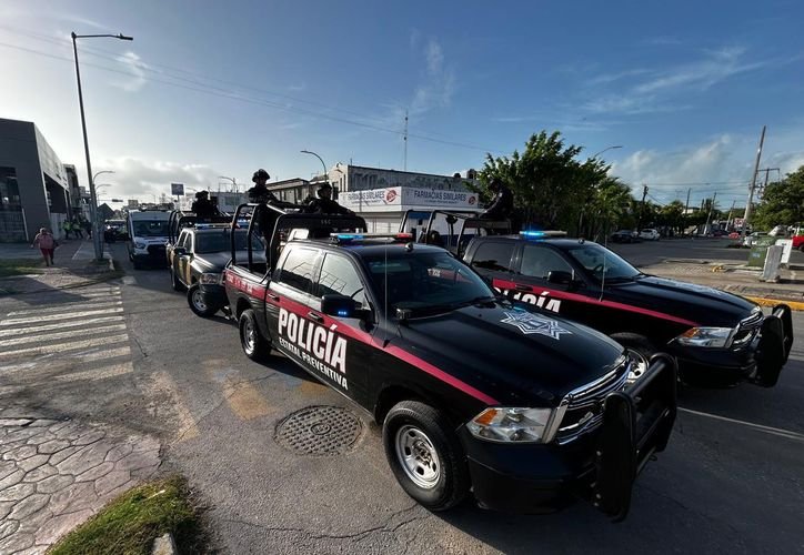 Two black police pickup trucks with red stripes and officers standing in the beds are parked on a paved street near a crosswalk and buildings.
