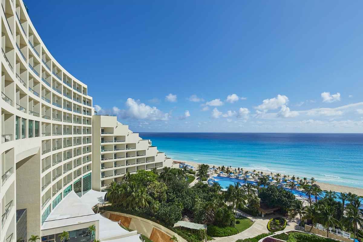 A panoramic view of a luxury resort with a beach and swimming pool, under a clear blue sky