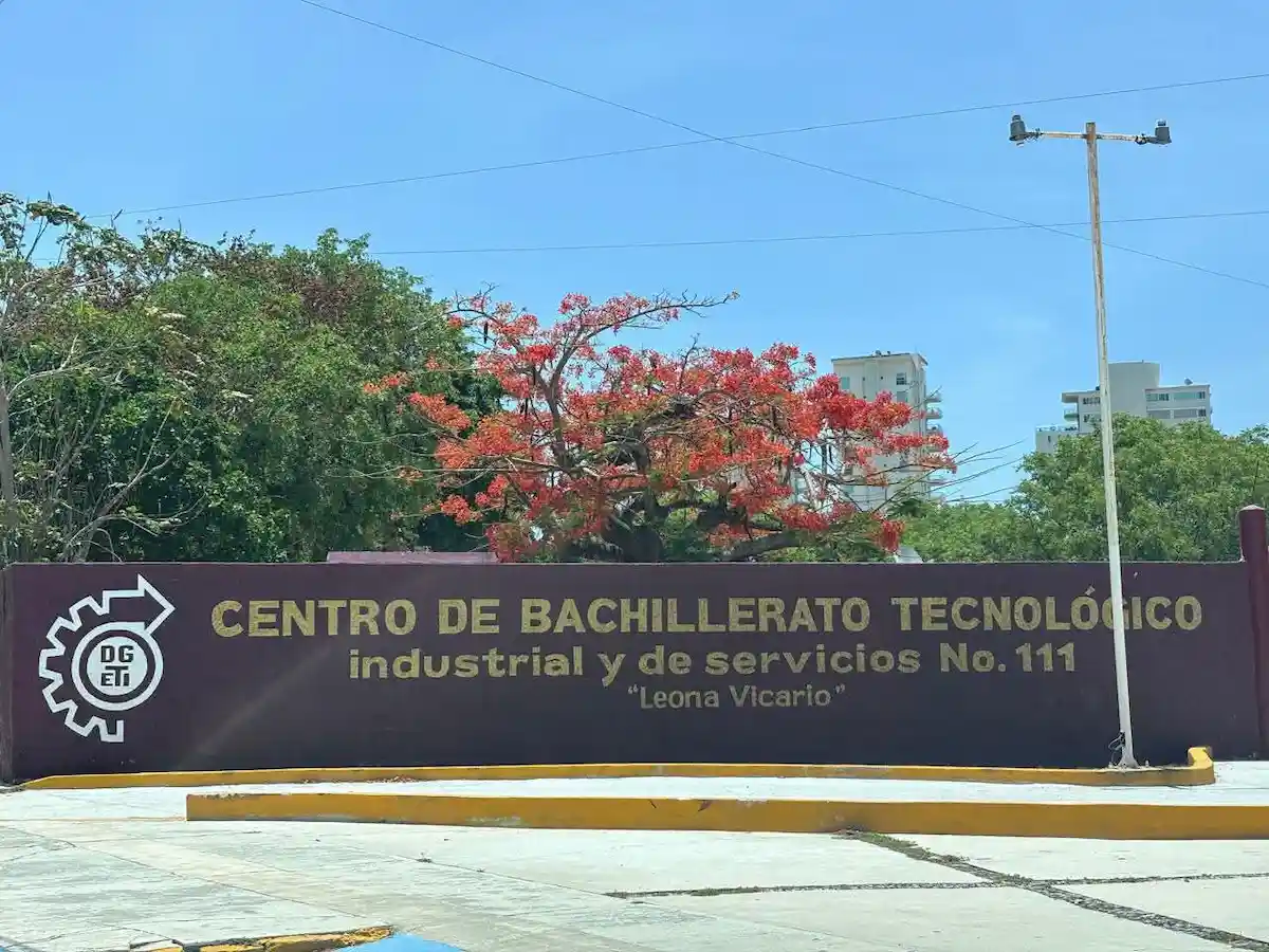 Sign of the Centro de Bachillerato Tecnológico industrial y de servicios No.111 "Leona Vicario" with trees and a clear blue sky in the background