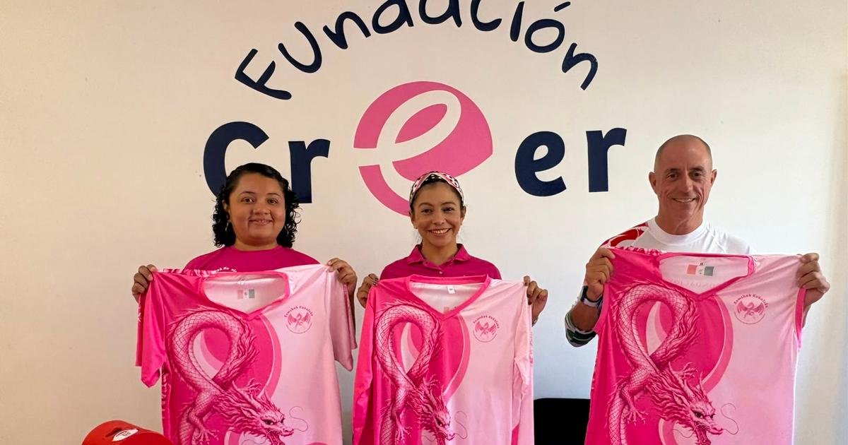 Three people stand in front of a wall with the words Fundación Creer and hold up pink shirts featuring a dragon design.