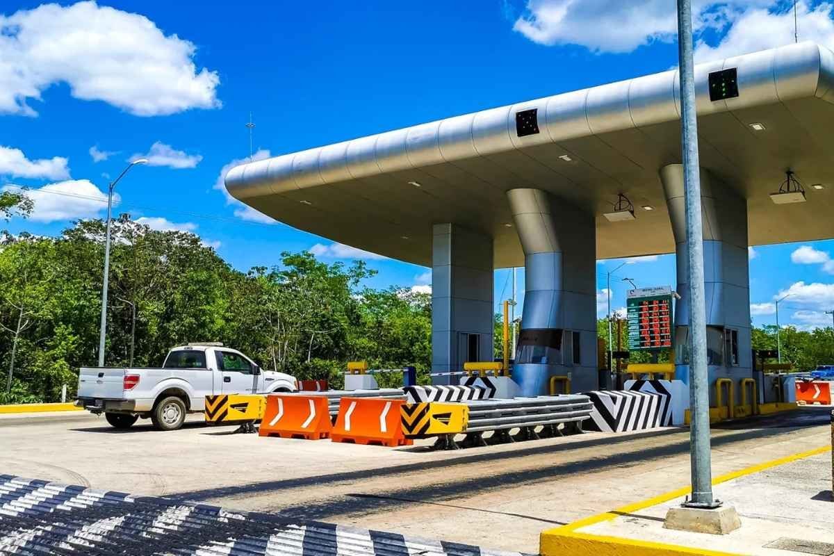 A modern toll plaza with a white truck at the entrance, surrounded by greenery and blue skies with fluffy clouds.$#$ CAPTION