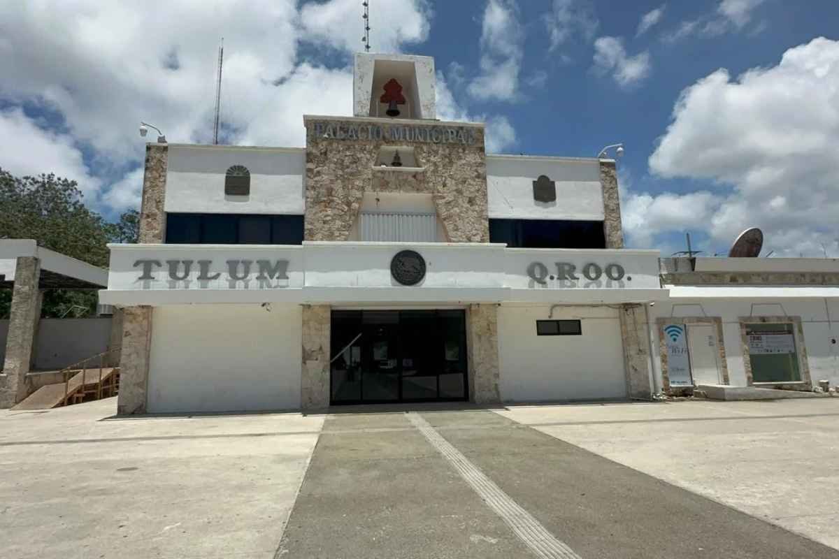 The exterior view of Tulum Municipal Palace, a modern building with stone accents, showcasing signage in both Spanish and English, under a partly cloudy sky.$# CAPTION