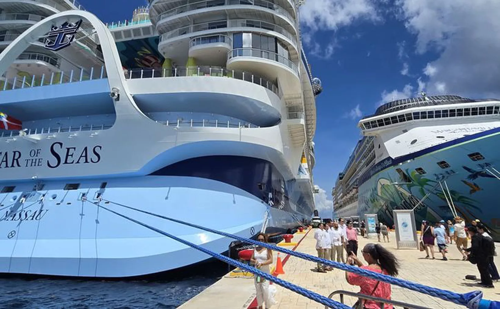 A large white cruise ship with the words Star of the Seas on its bow is docked beside a pier where people are walking, with a second cruise ship featuring colorful hull artwork visible on the right.