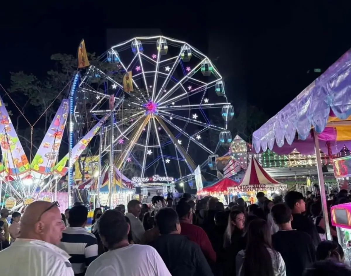 A bustling carnival scene at night, featuring a large illuminated ferris wheel and colorful stalls surrounded by crowds of people.$# CAPTION